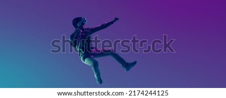Young Asian man wearing VR headset playing video game and levitating in the air on futuristic purple cyberpunk neon light banner background. Metaverse technology concept. Royalty-Free Stock Photo #2174244125