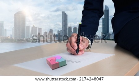 Businessman is signing documents containing puzzles, business solutions, success and strategic concepts. Cityscape background