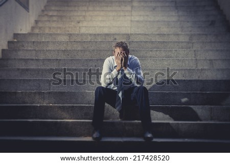 Young business man crying abandoned lost in depression sitting on ground street concrete stairs suffering emotional pain, sadness, looking sick in grunge lighting Royalty-Free Stock Photo #217428520