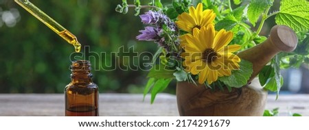 Alternative health medicine. Essential oil drop falling in a glass bottle, close up. Natural cosmetics, serum and vitamins. Fresh herbs in a mortar on a wooden table