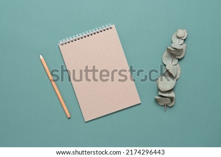 Empty brown notebook, pencil and eucalyptus branch. Turquoise pastel background. Top view, flat lay. Minimal workspace.