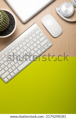Light wood desk and green paper background with wireless white mouse, white keyboard, headphone and professional camera, copy space for text, Top view, Flat lay.