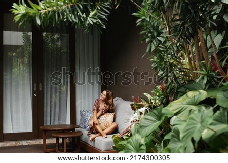 Young beautiful woman enjoys relaxing on the terrace of a resort hotel in Bali. Royalty-Free Stock Photo #2174300305