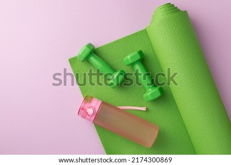 Sports accessories concept. Top view photo of green exercise mat dumbbells and pink bottle of water on isolated pastel lilac background