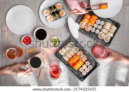 Three people play jenga with glasses of beer and wine with sets of rolls in which salmon, tobiko caviar, eel, cucumber, avocado, Philadelphia cheese, sesame seeds, wasabi, soy sauce and pickled ginger