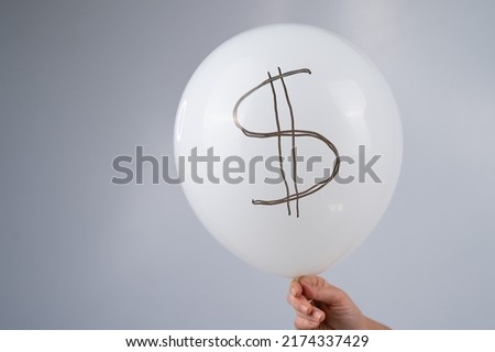 A woman is holding a balloon with a dollar sign. The concept of an inflated currency value.