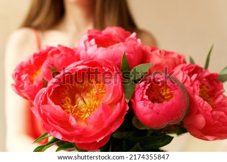 Nice young woman with bare shoulders holding a beautiful blossoming flower mono bouquet of fresh coral coloured peonies on beige background. Summer freshness, blossom, beauty concept