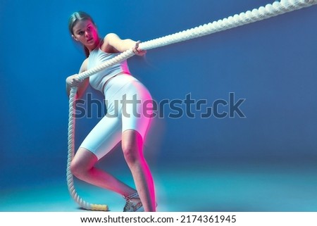 Modern strong sports girl pulling white rope training endurance in pink neon light. Long exposure. Fitness, wellness