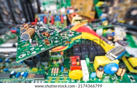 Circuit board on blur e-waste pile of discarded electric and computer devices. Air or ferrite core coils, chips or small components on cable TV amp PCB detail. Waste recycling in electronics industry. Royalty-Free Stock Photo #2174366799