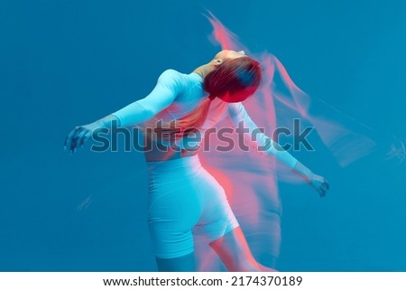 Sporty beautiful girl in white tracksuit dancing on blue background. Isolated fitness model in studio with motion blur effect.