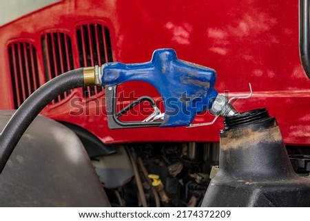 Diesel fuel nozzle fueling farm tractor. Farming input costs, fuel price increase and emissions pollution concept. Royalty-Free Stock Photo #2174372209