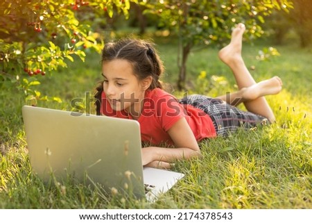 Beautiful young lady is chatting with friends outdoors as it is very useful to be in nature. Laptop is the best friend for a child nowadays. Green and vast meadow
