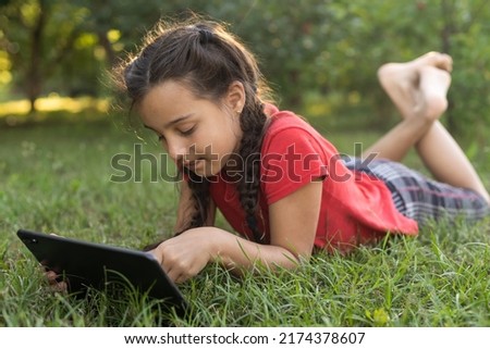 Child girl playing on a Digital tablet in the garden. Online or Remote education concept