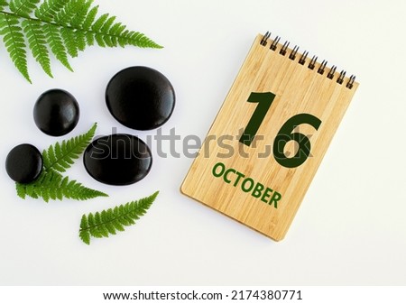 October 16. 16th day of the month, calendar date. Notepad, black SPA stones, green leaves. Autumn month, day of the year concep.