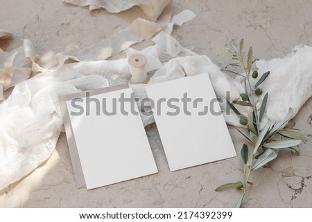 Mediterranean wedding stationery. Set of  greeting cards, invitations mock ups on beige marble background. Olive tree branches, silk ribbons with white muslin table runner. Summer design. Top view.