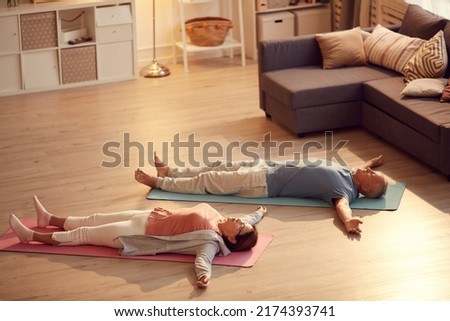 Tired senior couple lying with outstretched arms on floor while relaxing into Shavasana Royalty-Free Stock Photo #2174393741