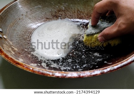 Human hand scrubbing or cleaning a burnt, scorched and greasy pan or wok on kitchen sink. Royalty-Free Stock Photo #2174394129