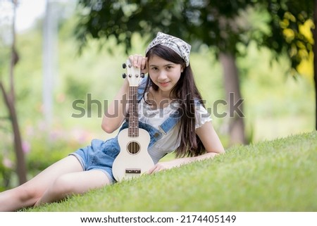 Portrait of Asian female sitting play the ukulele in park