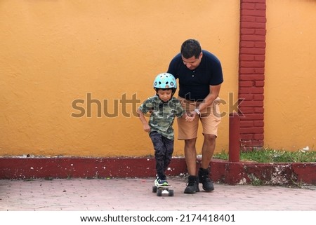 Latin single dad teaches his son to ride a skateboard with a helmet very funny and happy of the achievement of learning something new
