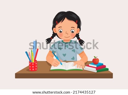 Cute little girl sitting on the desk studying writing on notebook doing her homework at home