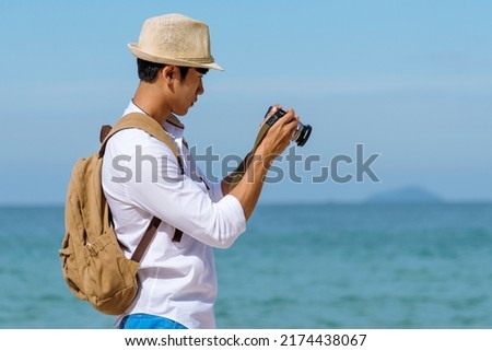 Man traveler using digital camera on summer beach blue sky take a photo. Asian Photographer man journey relax on the beach in summertime. Man backpack shooting photo asia destination holiday trip