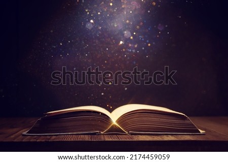 image of open antique book on wooden table with glitter overlay