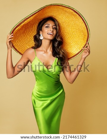 Woman in Big Summer Hat. Mexican Girl in Sombrero Hat. Fashion Model in Green Silk Dress over Yellow Studio Background. Women Vacation Clothes. Hair and Skin Sun Care Royalty-Free Stock Photo #2174461329