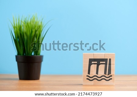 Ecology concept, wooden blocks with icon of dam hydroelectric reservoir floodgate renewable hydropower water, on blue background