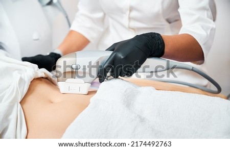 Close up view doctor's hands making non-invasive procedure of tightening abdomen skin, using sensor with micro-focused ultrasound spot heat layers of skin, up to musculoaponeurotic system SMAS. Royalty-Free Stock Photo #2174492763