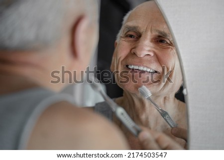 Smiling old man brushing his teeth prosthesis with toothbrush. Odontic healthcare concept. Royalty-Free Stock Photo #2174503547