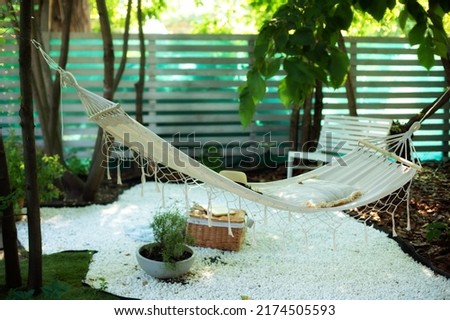 Hammock hanging hanging on tree in summer garden. Cozy exterior backyard. Hammock in boho style hanging on tree. Concept of recreation outdoor. Comfortable Cozy hygge place for weekend relax in yard. 