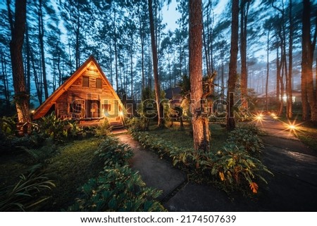 Pinewood cabin in pine forest green on nature trail. Wooden house or wooden hut along the Pinewood hill in twilight night Royalty-Free Stock Photo #2174507639