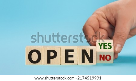 The word OPEN is written on wooden cubes. The hand turns the wooden cube and changes the word NO OPEN to YES OPEN