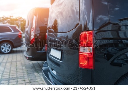 Close-up detail tail light view of many modern luxury black vans parked in row at car sale rental leasing dealer against sunset. Commericial trasfer cargo transportation company fleet. Vip charter Royalty-Free Stock Photo #2174524051