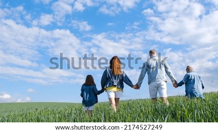 Happy family holding hands walking on a green field. Mom dad and daughter and son walk