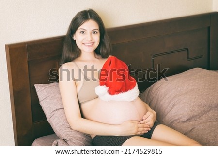 Pregnant in santa hat holding her belly. Christmas and New year concept.