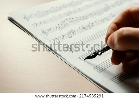 Treble and bass clef on a musical stand, recording notes, macro notes, notes with a female hand holding an ink pen in the background