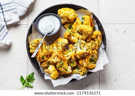 Baked spicy cauliflower wings with yogurt sauce in a black plate, top view. Vegan diet recipe concept. Royalty-Free Stock Photo #2174536271