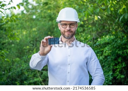 Businessman man in hardhat showing blank business card outdoors, copy space