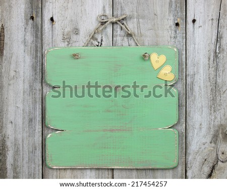 Blank green sign with gold hearts hanging on weathered wooden fence