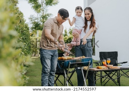Asian family having dinner in the backyard at home. Happy family with little child camping and have fun in house backyard outside. Barbecue time, Family activities conccept. Royalty-Free Stock Photo #2174552597