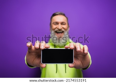 pleased senior man with beard and grey hair holding smartphone with blank screen on purple