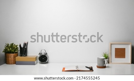 Contemporary workplace with alarm clock, books, potted plant and picture frame on white table. Copy pace for your advertise text