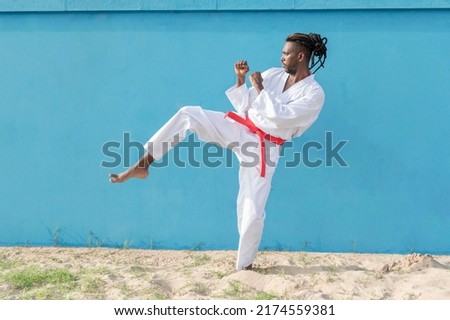 a young african american man training taekwondo outdoors kicking on a blue background