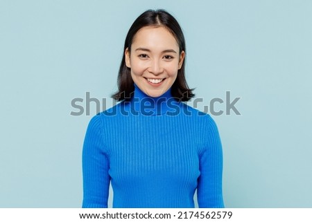 Smiling fancy fascinating young woman of Asian ethnicity 20s years old wears blue shirt looking camera isolated on plain pastel light blue background studio portrait. People emotions lifestyle concept Royalty-Free Stock Photo #2174562579