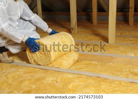 Construction worker thermally insulating house attic with glass wool  Royalty-Free Stock Photo #2174573103