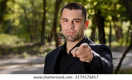 Cheerful confident adult businessman guy show hey you gesture points finger at camera make best choice handsome caucasian man wears formal suit stand outdoors nods head choose option approve good idea