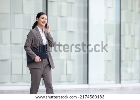 Asian woman with smartphone walking against street blurred building background, Fashion business photo of beautiful girl in casual suite with smart phone.
