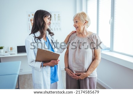 Happy senior woman visiting doctor and listening to her advice during appointment. Nurse Showing Patient Test Results On Clipboard. Doctor and patient standing in doctor's office