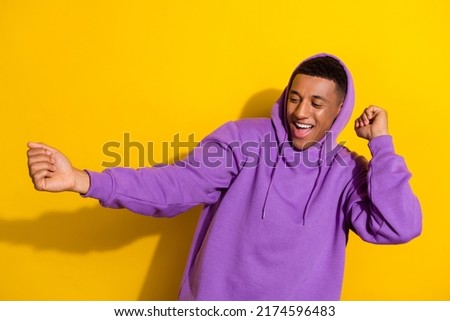 Photo of confident handsome young man dancing dubstep in purple hoodie isolated on yellow color background
